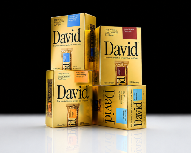 Gold cardboard boxes of David protein bars stacked against a dark background, each printed with 28g Protein, 150 Calories and 0g Sugar