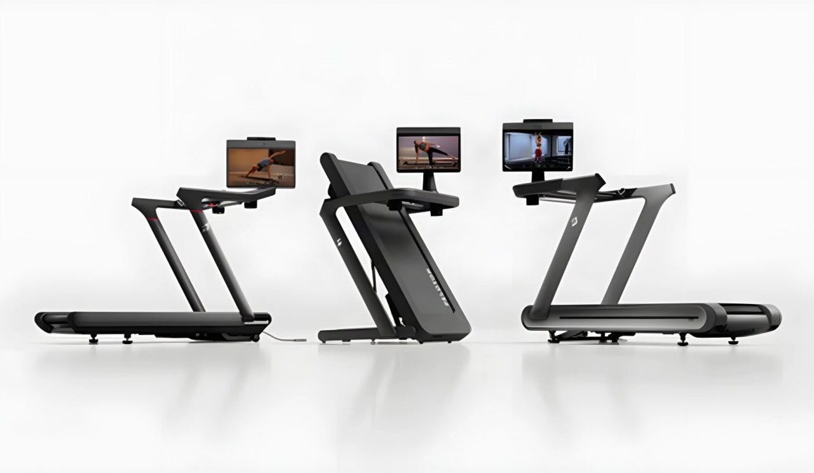 Three Peloton treadmills side by side, the centre one folded upright, each with a touchscreen showing a workout