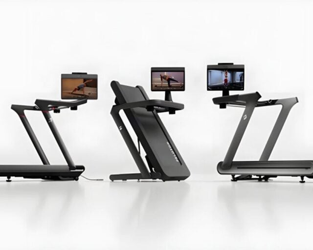 Three Peloton treadmills side by side, the centre one folded upright, each with a touchscreen showing a workout
